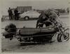 Firefighter examining motorcycle involved in accident, I-91, Hartford, May 18, 1976